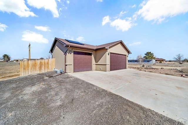 view of property exterior with driveway, solar panels, an attached garage, fence, and stucco siding