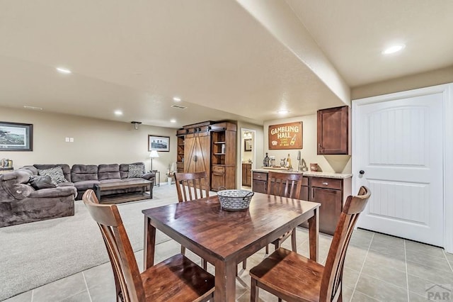 dining room featuring light tile patterned floors, a barn door, light colored carpet, and recessed lighting