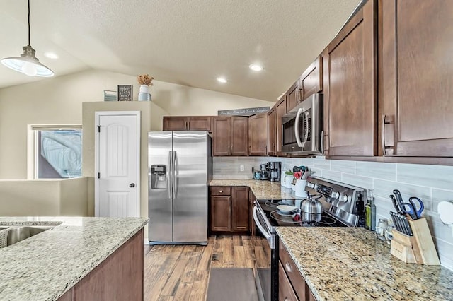 kitchen featuring vaulted ceiling, light stone counters, stainless steel appliances, and wood finished floors