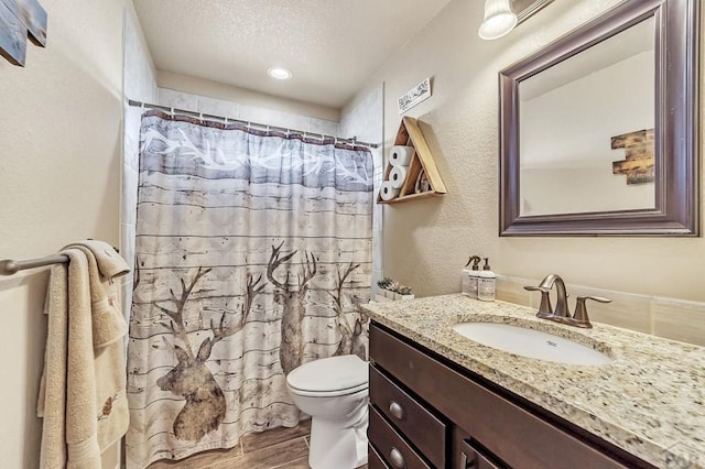 full bathroom featuring a textured wall, toilet, vanity, a textured ceiling, and wood finished floors