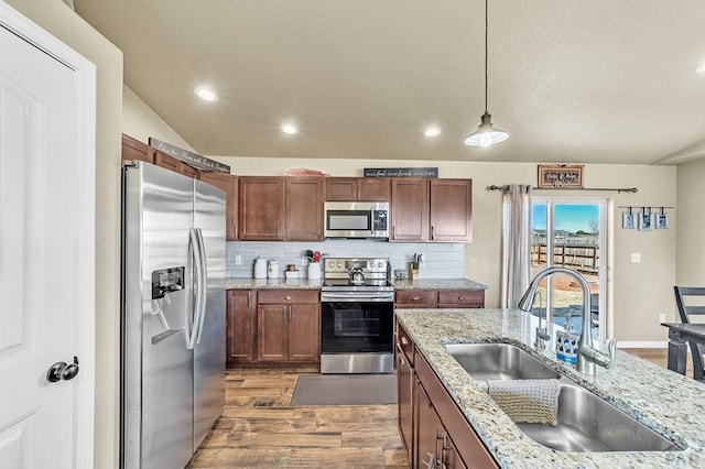 kitchen with stainless steel appliances, lofted ceiling, backsplash, a sink, and wood finished floors