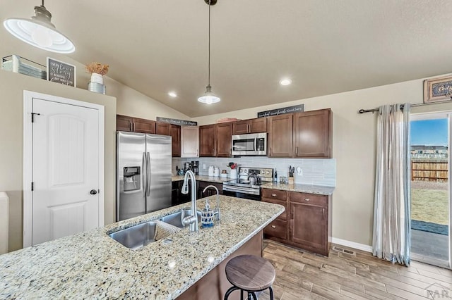 kitchen featuring decorative light fixtures, backsplash, appliances with stainless steel finishes, vaulted ceiling, and a sink