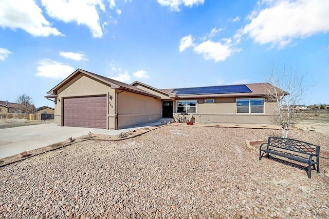 ranch-style home with a garage, concrete driveway, roof mounted solar panels, and stucco siding