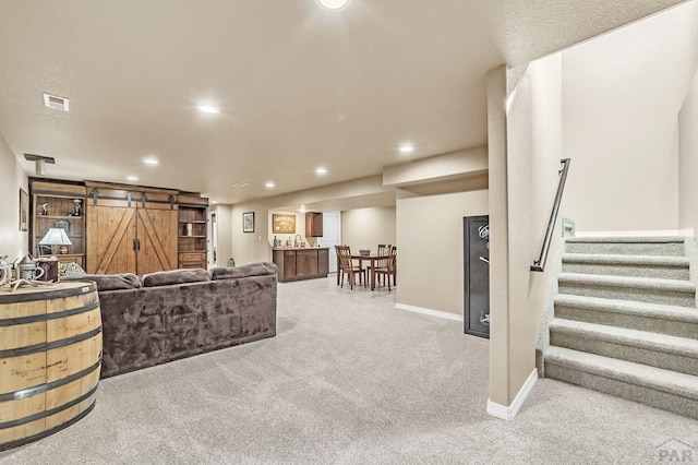 living area featuring a barn door, light colored carpet, recessed lighting, visible vents, and stairway