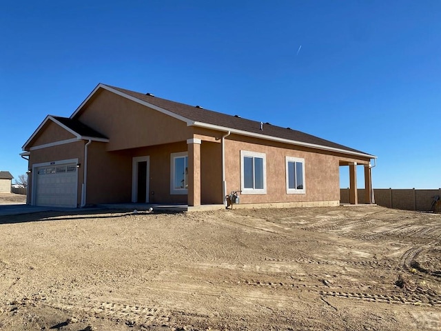 rear view of house with a garage, fence, and stucco siding