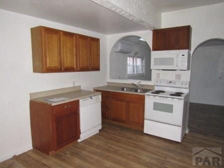 1119 Pine St, Pueblo, CO 81004 - kitchen with white appliances, a sink, dark wood-style floors, brown cabinetry, and arched walkways