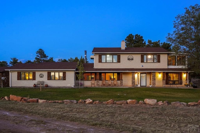 view of front of house with brick siding, a yard, and a chimney