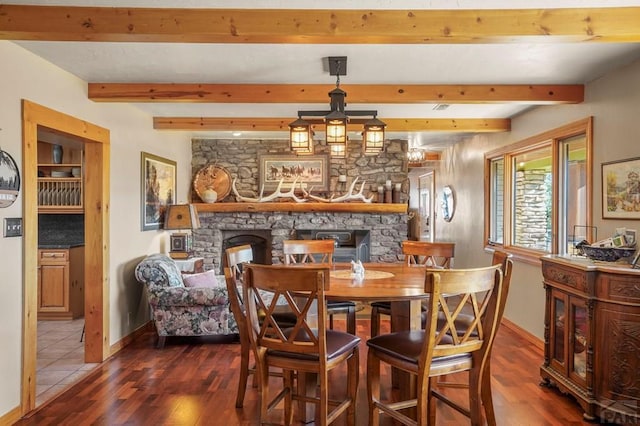 dining area featuring baseboards, dark wood-type flooring, beam ceiling, and a stone fireplace