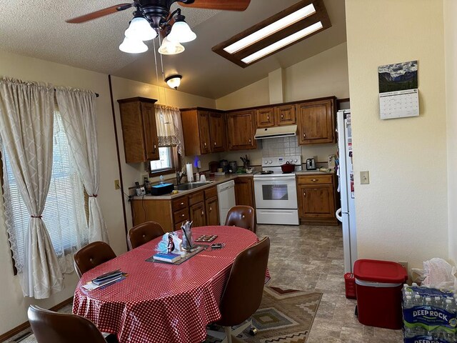 kitchen with lofted ceiling, under cabinet range hood, white appliances, light countertops, and brown cabinetry