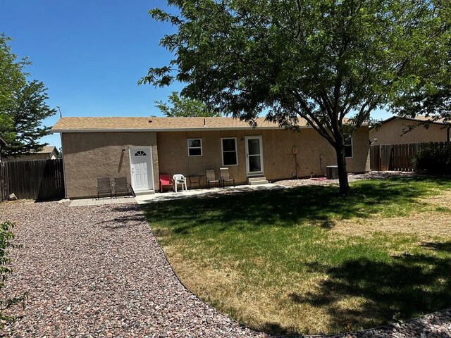 back of house with entry steps, a lawn, fence, and stucco siding