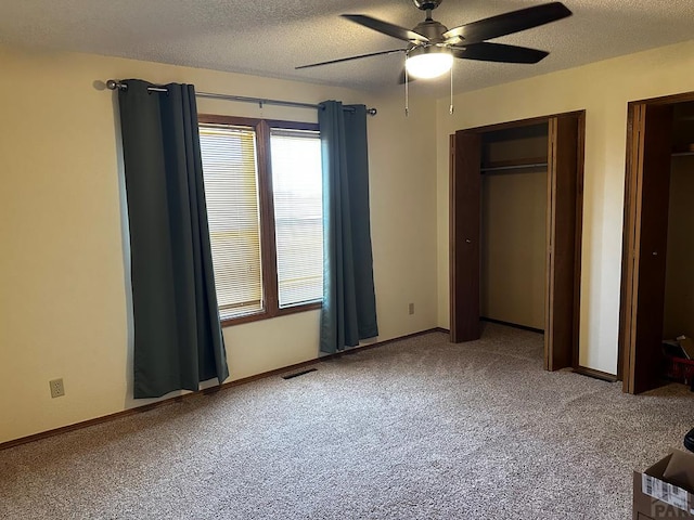 unfurnished bedroom featuring a textured ceiling, carpet flooring, visible vents, baseboards, and multiple closets