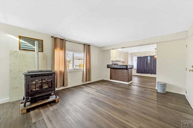 unfurnished living room with dark wood-type flooring, a dry bar, a wood stove, and baseboards