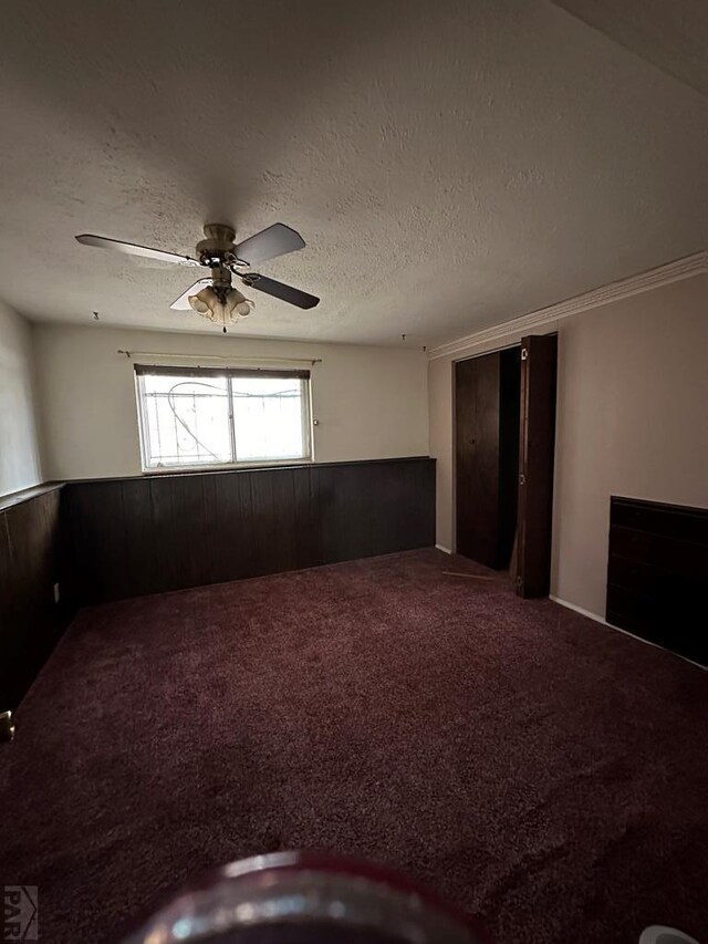 carpeted spare room with a textured ceiling, wainscoting, a ceiling fan, and wooden walls