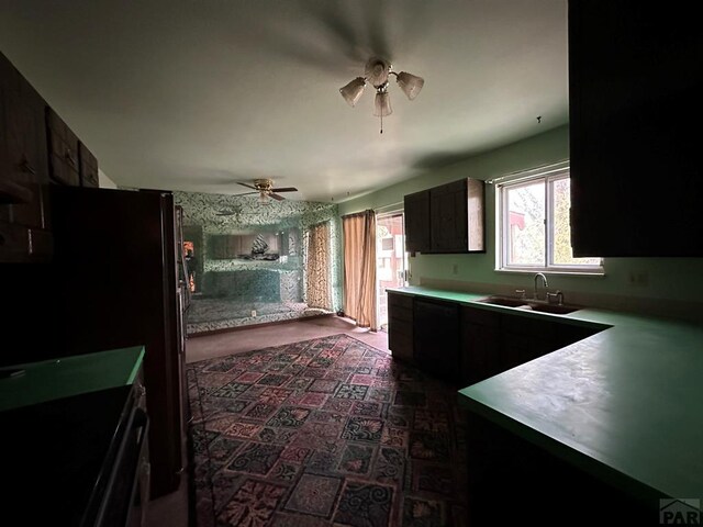 kitchen featuring light countertops, a ceiling fan, freestanding refrigerator, a sink, and dark brown cabinetry