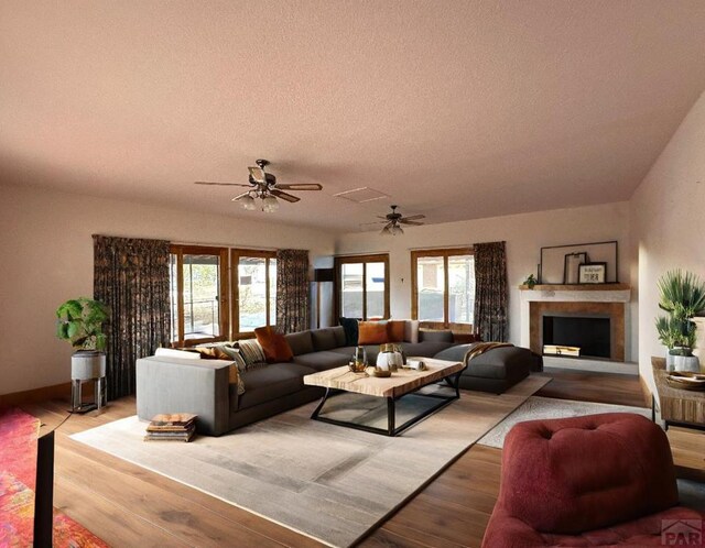 living room with a ceiling fan, light wood-type flooring, a fireplace, and a textured ceiling