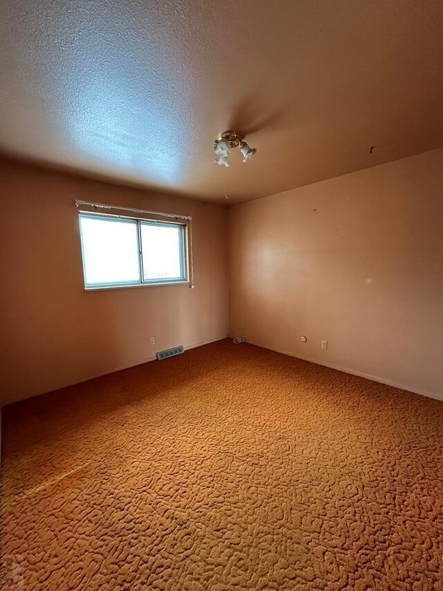 carpeted empty room with a textured ceiling and visible vents