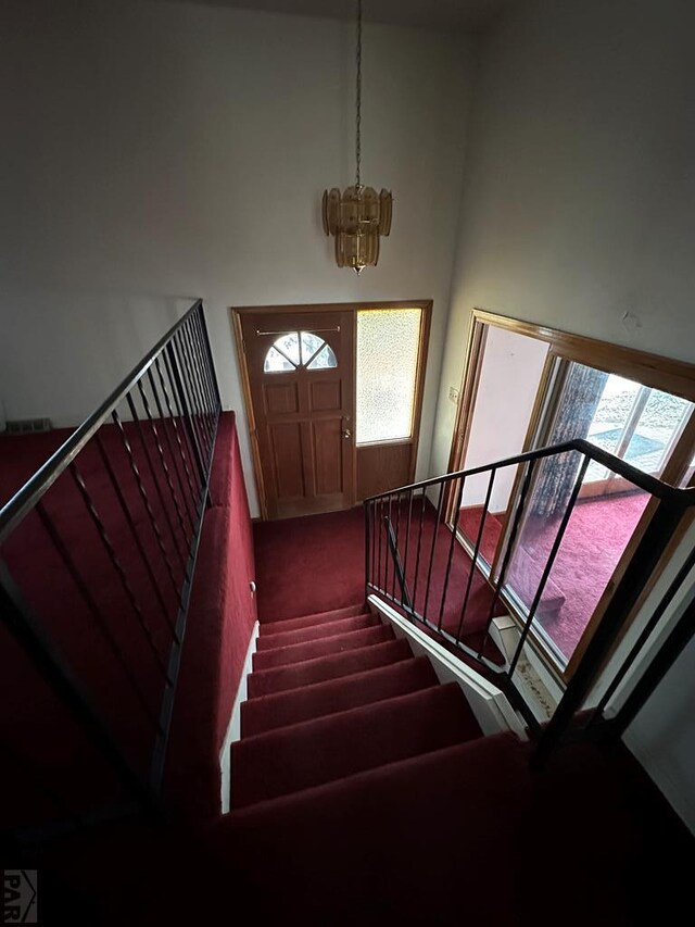 stairs featuring carpet floors, a notable chandelier, and a towering ceiling