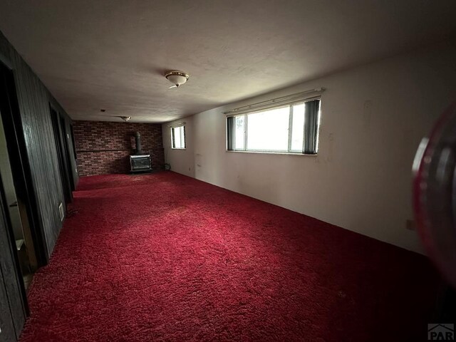 carpeted spare room with brick wall and a wood stove