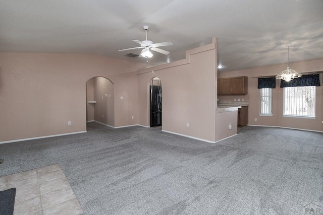 unfurnished living room with arched walkways, carpet flooring, ceiling fan with notable chandelier, and visible vents