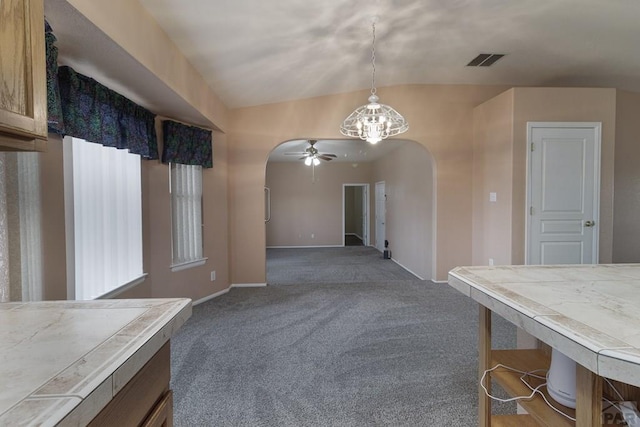 unfurnished dining area with a ceiling fan, visible vents, lofted ceiling, arched walkways, and dark colored carpet