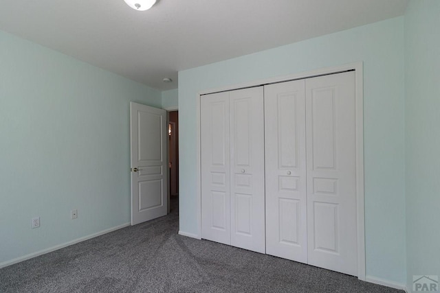 unfurnished bedroom featuring baseboards, dark colored carpet, and a closet