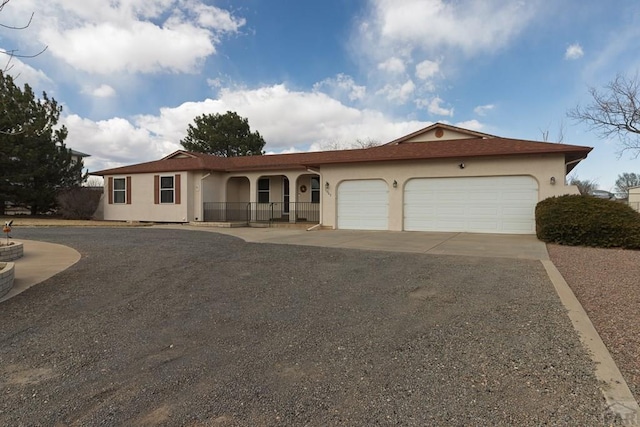 ranch-style home featuring stucco siding, a garage, covered porch, and driveway