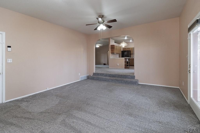 unfurnished living room featuring arched walkways, ceiling fan, baseboards, and carpet