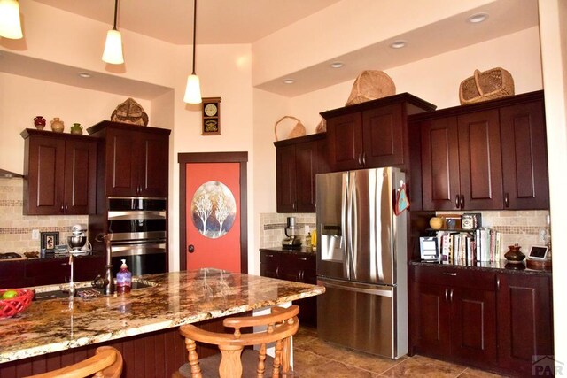 kitchen with dark stone counters, decorative backsplash, hanging light fixtures, stainless steel appliances, and a kitchen bar