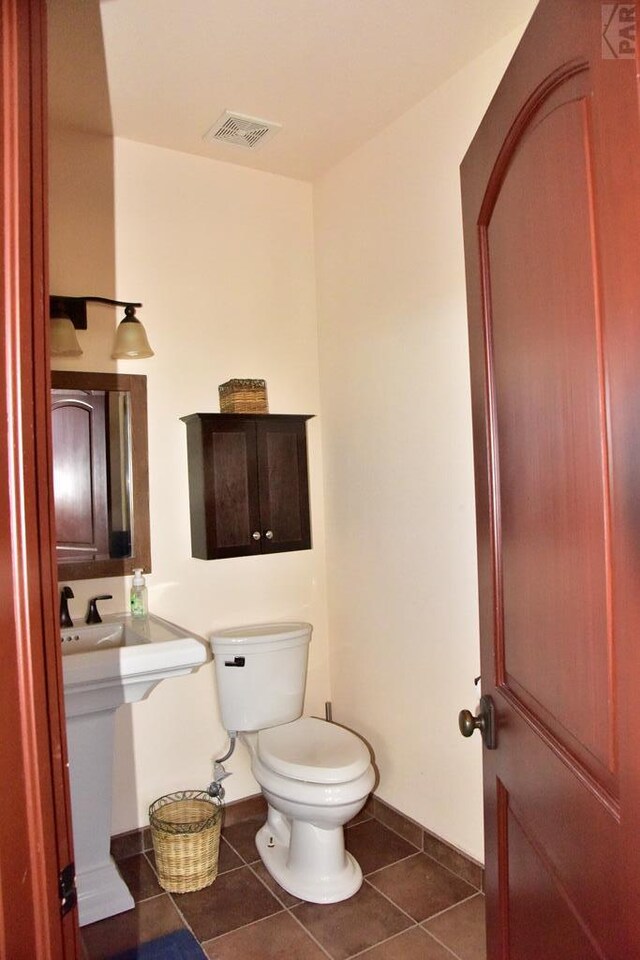 half bath featuring toilet, tile patterned flooring, visible vents, and baseboards