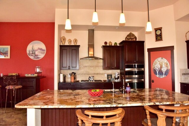 kitchen featuring stainless steel double oven, backsplash, wall chimney range hood, and a kitchen bar