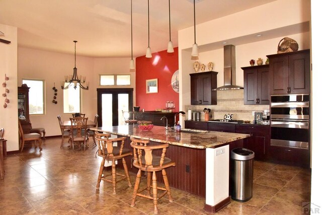 kitchen with wall chimney exhaust hood, appliances with stainless steel finishes, a breakfast bar area, a sink, and backsplash