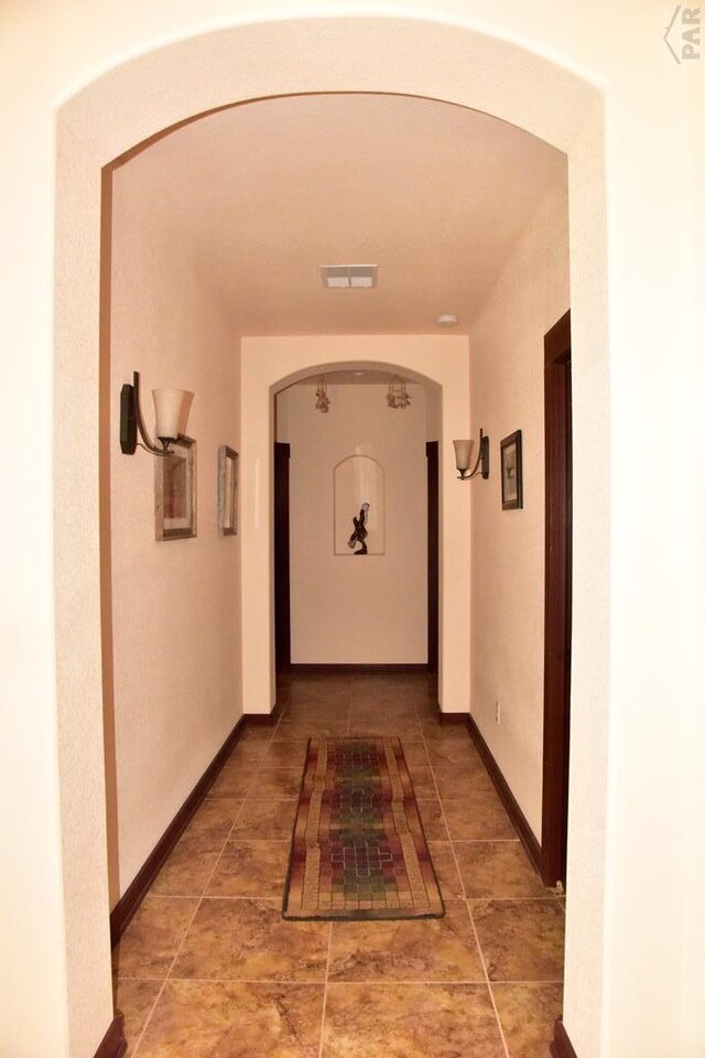 hallway featuring arched walkways, visible vents, and baseboards