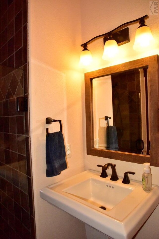 bathroom with tiled shower and a sink