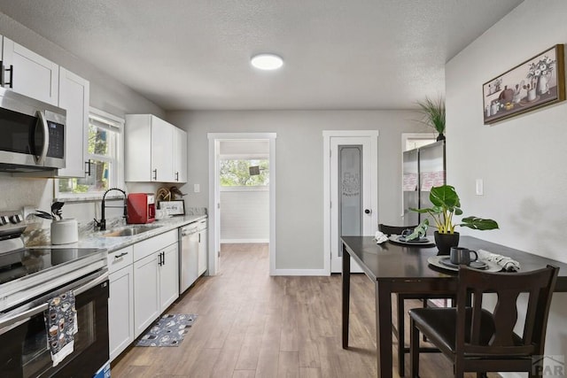1934 E 11th St, Pueblo, CO 81001 - kitchen with stainless steel appliances, a sink, white cabinetry, light wood-style flooring, and a textured ceiling