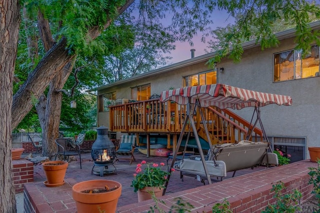 back of property at dusk with a patio, a wooden deck, an outdoor fire pit, stucco siding, and stairway