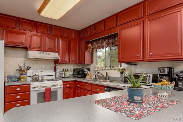 kitchen featuring tasteful backsplash, under cabinet range hood, light countertops, a sink, and white range with gas stovetop