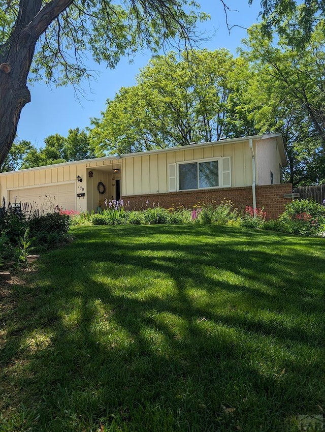 ranch-style house featuring board and batten siding, fence, brick siding, a front lawn, and a garage