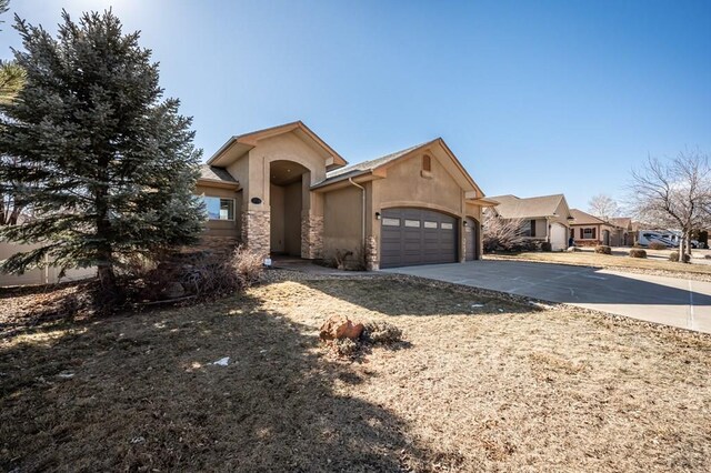 view of front of house featuring a garage, driveway, stone siding, and stucco siding