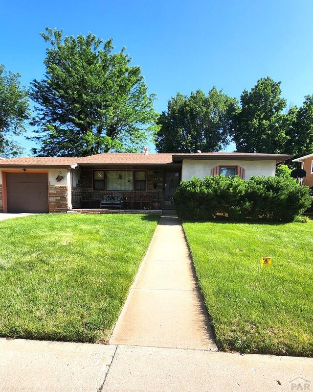 3219 Urban St, Pueblo, CO 81005 - ranch-style house featuring a front lawn, an attached garage, covered porch, and stucco siding