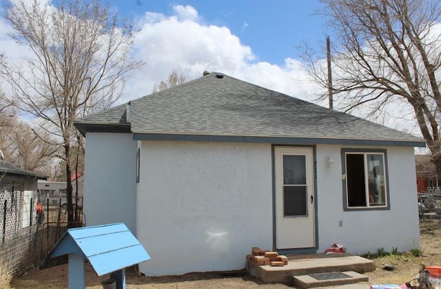 rear view of house featuring roof with shingles, fence, and stucco siding