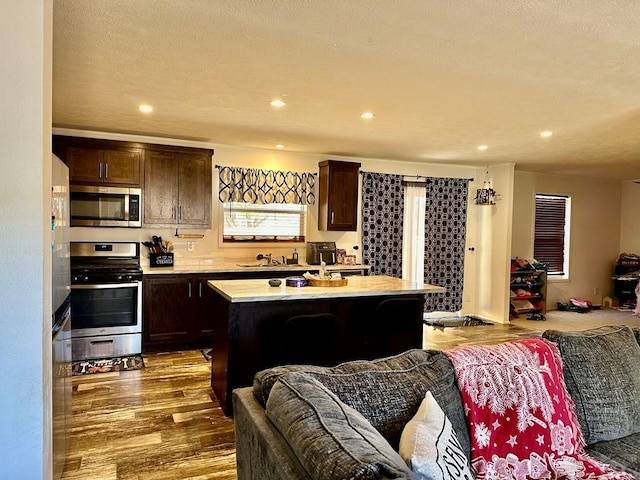 kitchen featuring stainless steel appliances, light countertops, dark wood-type flooring, open floor plan, and a kitchen island