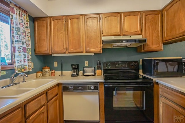 kitchen with brown cabinets, light countertops, a sink, under cabinet range hood, and black appliances