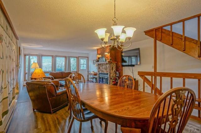 dining area featuring a baseboard radiator, wood finished floors, an inviting chandelier, a textured ceiling, and a fireplace