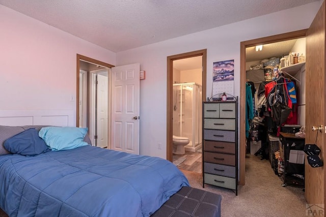 bedroom featuring a textured ceiling, ensuite bathroom, light colored carpet, a spacious closet, and a closet