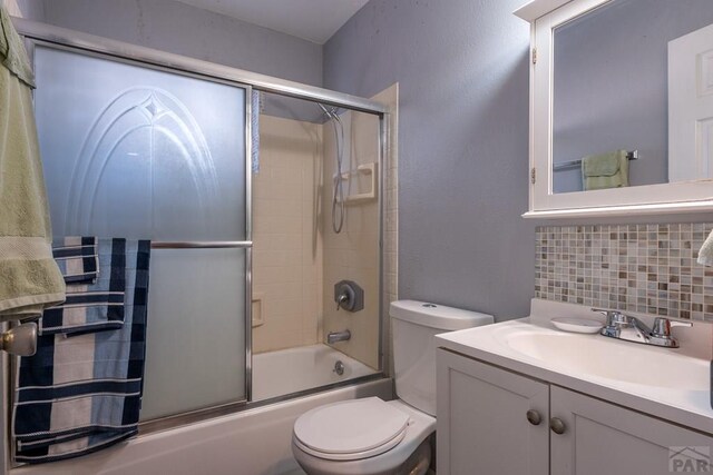 bathroom featuring enclosed tub / shower combo, toilet, vanity, and decorative backsplash