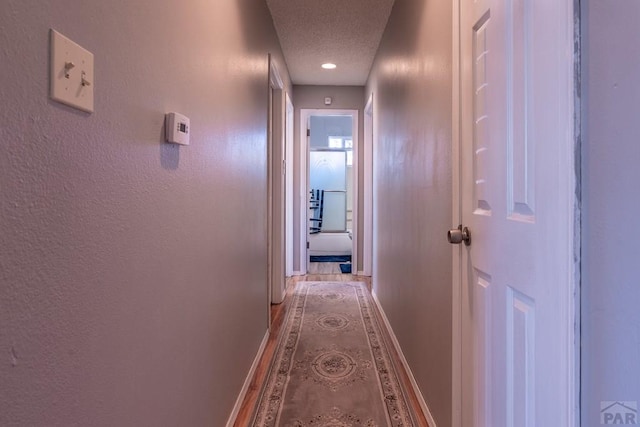 hall with light wood-style floors, a textured wall, a textured ceiling, and baseboards