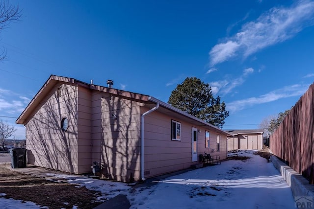 view of snowy exterior with an outbuilding, a storage unit, and fence