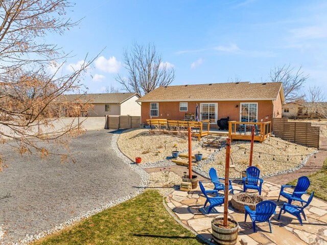 rear view of property with an outdoor fire pit, fence, and stucco siding