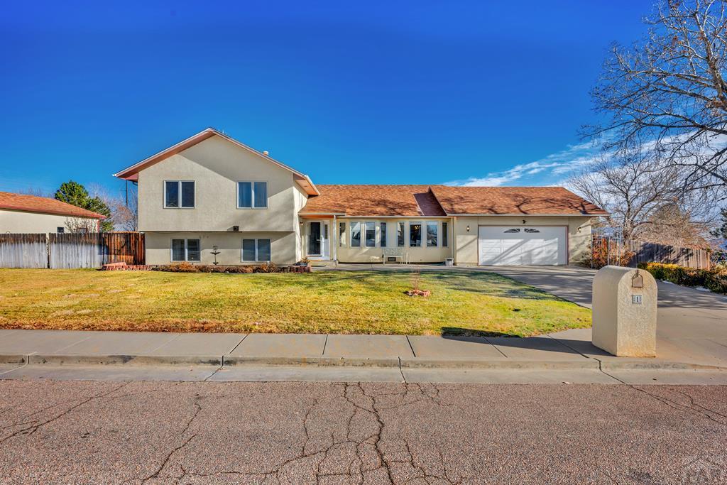 split level home featuring an attached garage, fence, concrete driveway, stucco siding, and a front yard