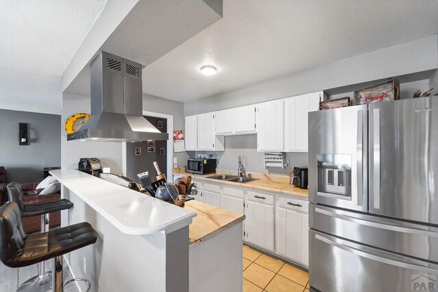 kitchen featuring a breakfast bar, island exhaust hood, light countertops, appliances with stainless steel finishes, and white cabinetry